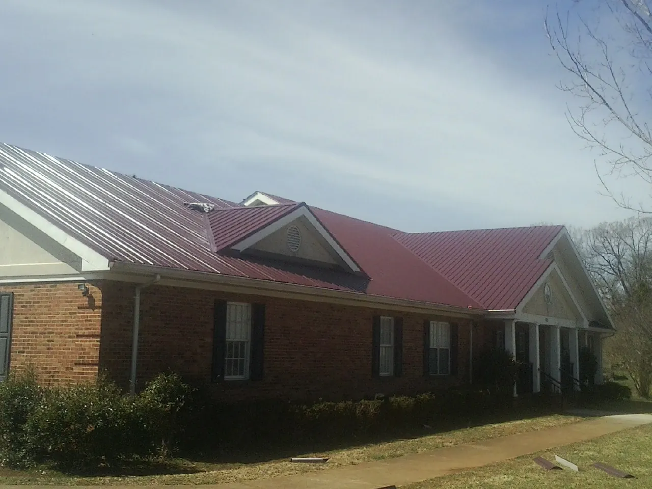 Red metal roof with gabled entries on a long brick building, from a Hail Damage Roof Repair job in Hunt Valley