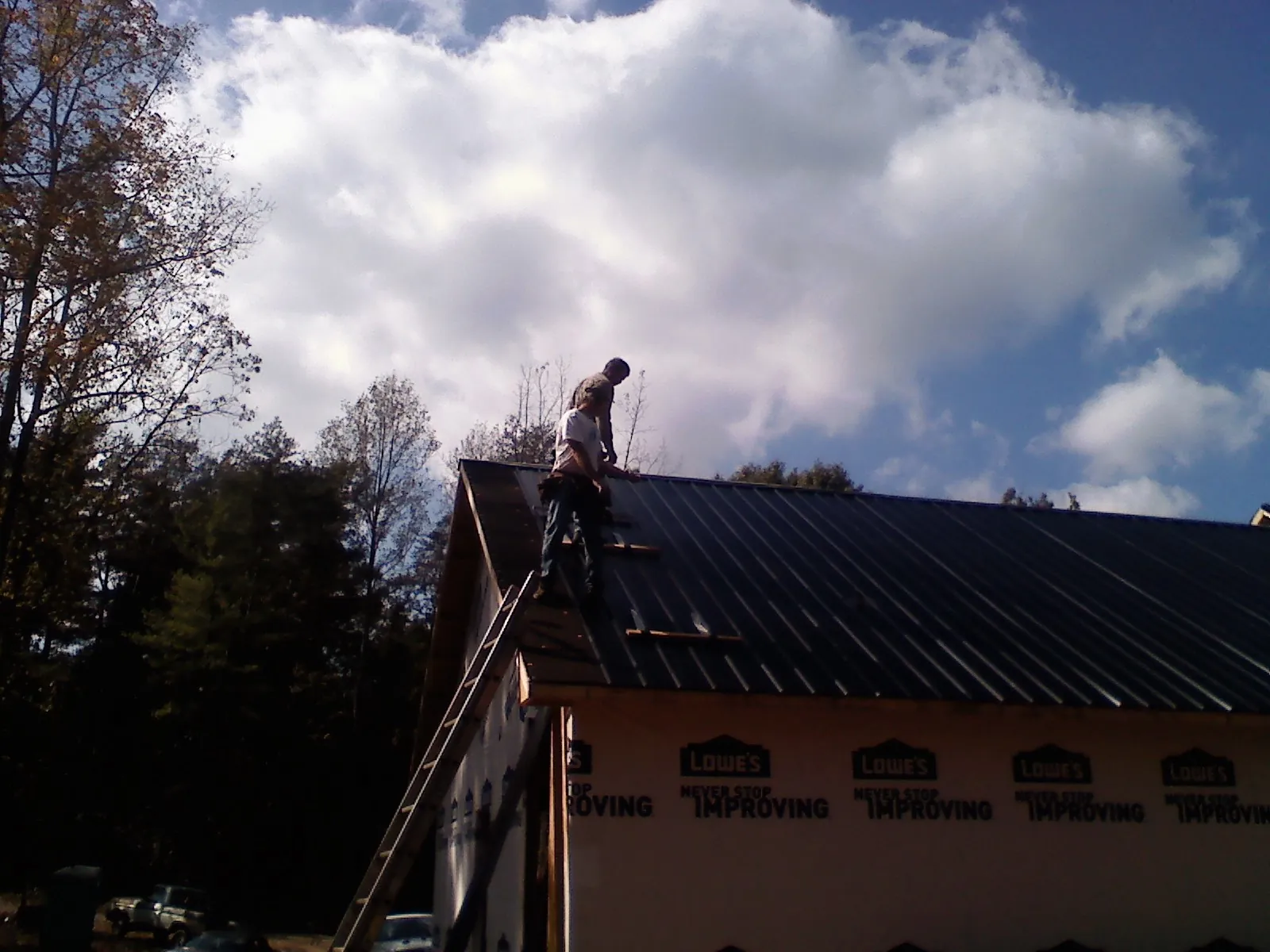 Roofer fastening dark metal panels high against a cloudy sky, from a Roof Inspection job in Hunt Valley