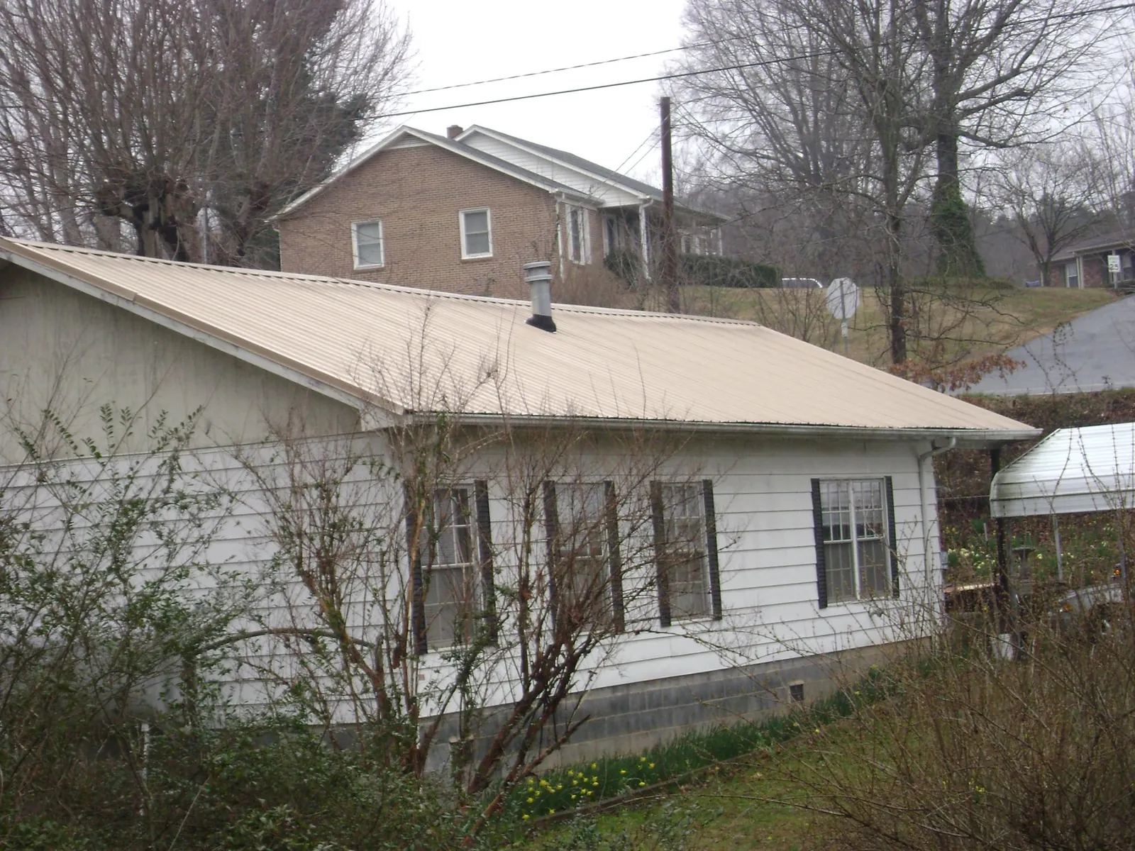 Tan metal roof on a white sided house set into a hillside — Commercial Roofing by Roofing Brothers in Hunt Valley